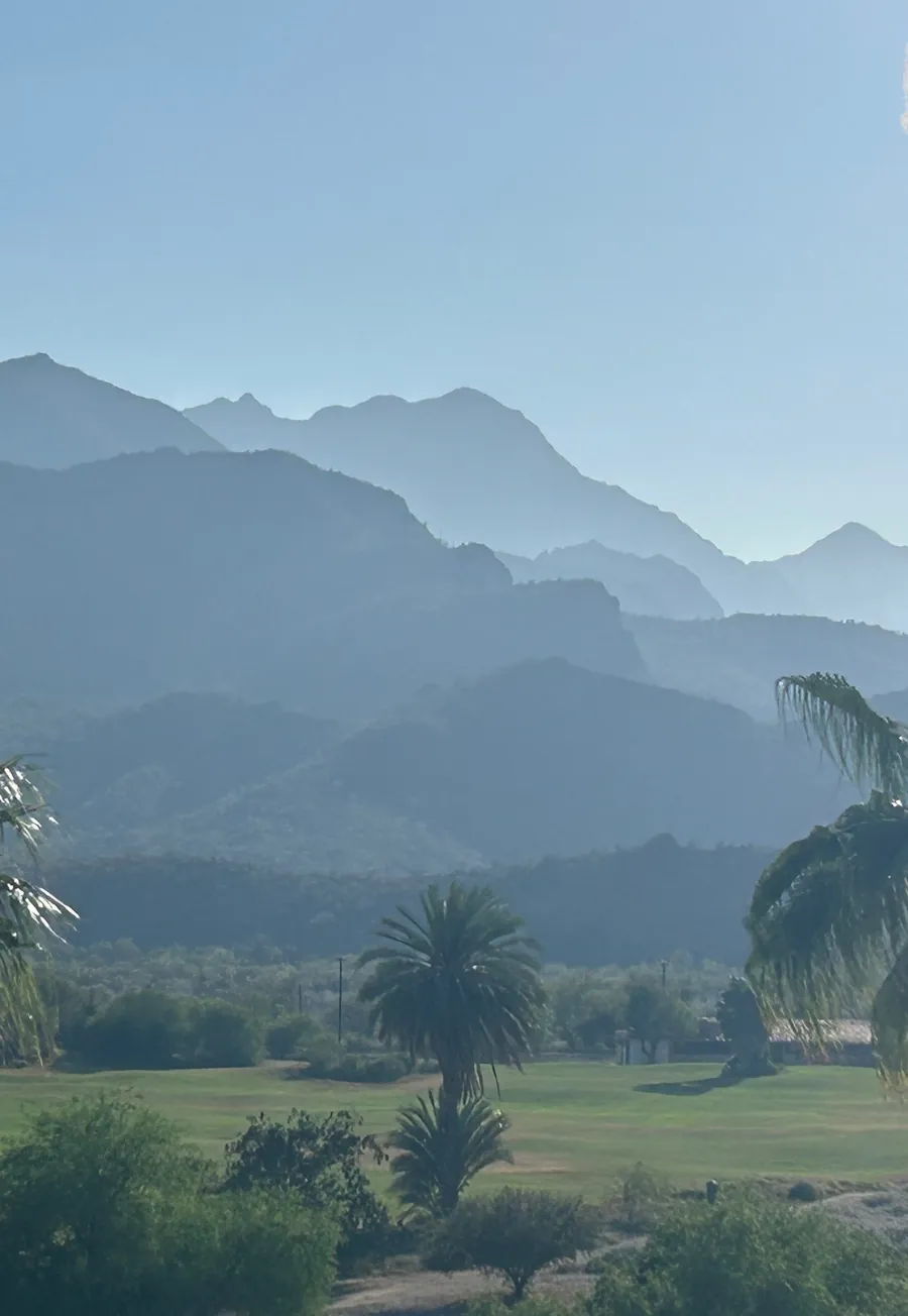 Layered blue mountains behind palm trees and green grounds at Loreto Bay